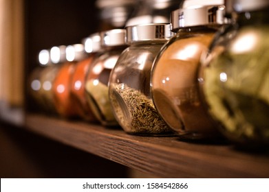 Spice Jars On A Shelf In Kitchen Being Displayed Inline, Paprika, Pepper, Spices, Rosemary, Basil, Curry. Focus Is Done On Rosemary.