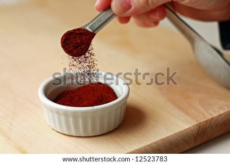 Spice measured with measuring spoon into ramekin on cutting board