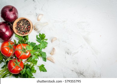 Spices (black pepper, garlic, onion), greens and tomatoes. Ingredients for cooking. On the white stone concrete table top view copy space 