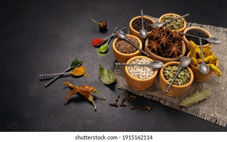 Spices and condiments in spoons and bowls for cooking on black background