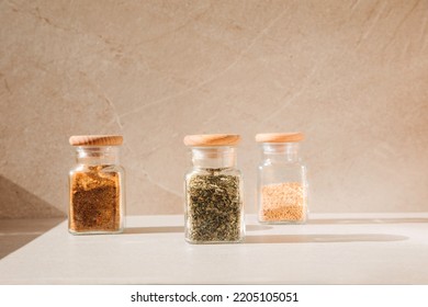 Spices in glass jars on a light stone background with shadows. Paprika, herbs, mustard, front view