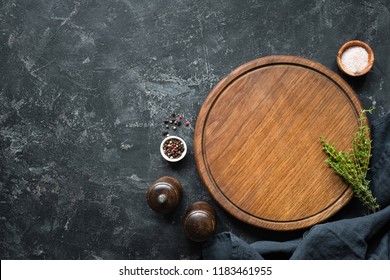 Spices, Herbs, Cutting board for cooking. Round wooden cutting board on black concrete backdrop. Top view with copy space for text. Menu, recipe mock up, banner background