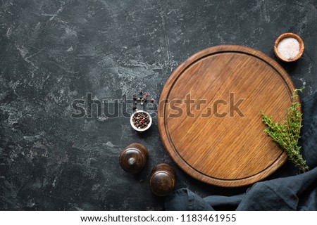 Spices, Herbs, Cutting board for cooking. Round wooden cutting board on black concrete backdrop. Top view with copy space for text. Menu, recipe mock up, banner background