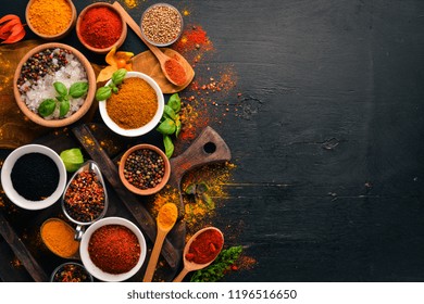 Spices and herbs on a wooden board. Pepper, salt, paprika, basil, turmeric. On a black wooden chalkboard. Top view. Free copy space. - Powered by Shutterstock