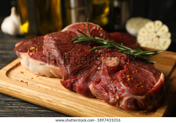Spices, oil and board with raw steak meat on\
wooden background