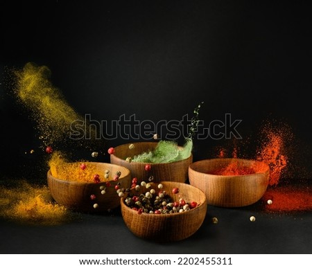 Spices and seasonings powder splash, explosion. Set of colorful spices in wooden bowls, isolated on black background. Freeze motion photo