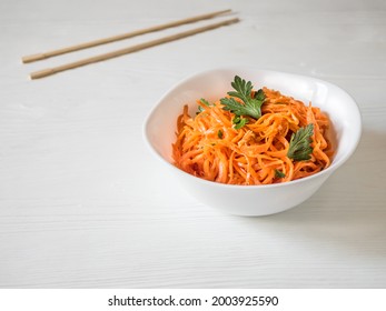Spicy Asian salad with grated carrots and parsley. Korean carrots in a white bowl with chopsticks on a white plate. Vegetarian diet. Healthy food concept. Horizontal. Copy space