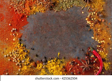 Spicy background with assortment of different hot chili and allspice peppers and mix of other spices over old rusty iron background. Top view. With space for text