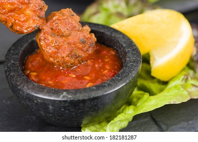 Spicy Chicken Satay - Marinated chicken meatball skewers served with chilli sauce and lemon wedges on a slate with reflections.
