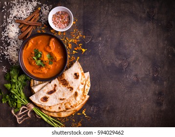 Spicy chicken tikka masala in bowl on rustic wooden background. With rice, indian naan butter bread, spices, herbs. Space for text. Traditional Indian/British dish. Top view. Indian food. Copy space