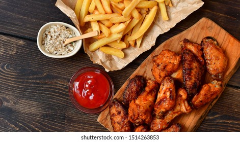 Spicy Chicken Wings And French Fries. Food Lunch Or Dinner, Typical Fast Food. On A Wooden Background. Food Delivery Concept. Selective Focus And Copy Space