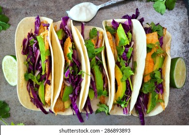Spicy fish tacos with red cabbage lime slaw and avocado, overhead view on rustic tray
