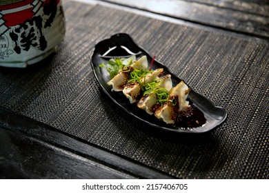Spicy fried pork gyoza dumplings with salad in the traditional Japanese ramen restaurant, with a black plate on a black mat and Japanese fonts sake barrel translation: Invincible Great Gate