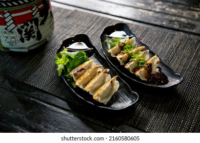 Spicy fried pork gyoza dumplings with salad combo in the traditional Japanese ramen restaurant, with a black plate on a black mat and Japanese fonts sake barrel translation: Invincible Great Gate