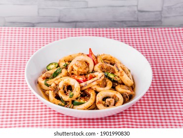 Spicy fried squid with basil leaves on dinner table background