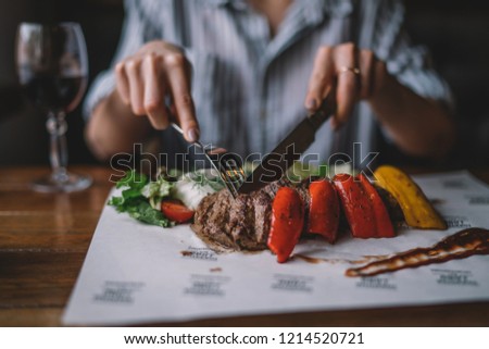 Spicy grilled lamb leg with vegetables and herbs on a roasting cast iron. Barbecue lamb with vegetables. Healthy food. Eating and leisure concept. Woman having dinner at table with food. Toned image.