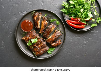 Spicy hot grilled spare ribs on plate over black stone background. Tasty bbq meat. Top view, flat lay