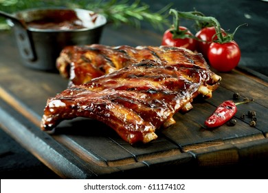 Spicy hot grilled spare ribs from a summer BBQ served with a hot chili pepper and fresh tomatoes on an old vintage wooden cutting board - Shutterstock ID 611174102