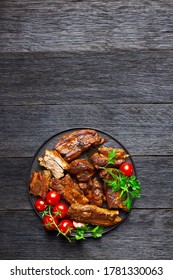 Spicy Korean Slow-cooked Pork Ribs With Red Pepper Flakes, Cherry Tomato, And Parsley On A Black Plate On A Dark Wooden Background, Top View, Copy Space