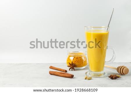 Spicy latte in a tall glass, golden moon milk with turmeric, honey and cinnamon. Close-up, horizontal with space