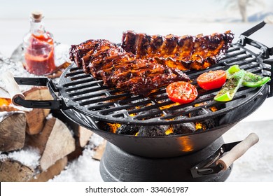 Spicy marinated spare ribs grilling outdoors on a portable barbecue standing in a snowy winter landscape during a seasonal, festive grill party