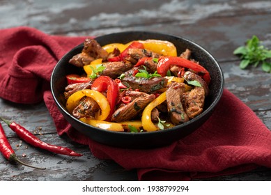 Spicy Meat With Peppers Cooked In A Wok. Pieces Of Chicken With Red And Yellow Peppers In A Black Bowl On A Dark Background. Asian Style Food.