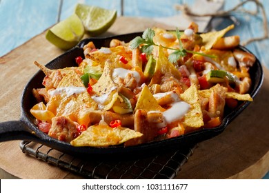 Spicy Mexican chicken with nachos and fresh herbs drizzled with cream and served in a rustic skillet in a close up view
