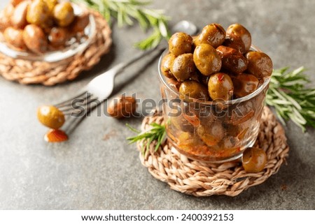Spicy olives in a glass bowl. Bowl with preserved olives and rosemary twigs on a stone table.