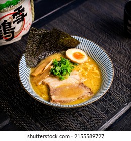 Spicy pork tonkotsu chashu ramen in the traditional Japanese ramen restaurant, with a ramen bowl on a black mat and Japanese fonts sake barrel translation: Snow Crane