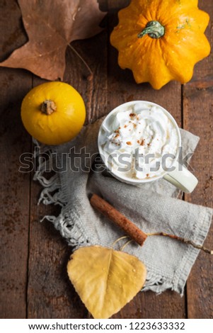 Spicy pumpkin latte with cinnamon and autumn leaves on wooden background