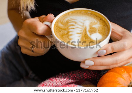 Spicy pumpkin latte on a wooden board with  autumn leaves. Cup with young woman hands.