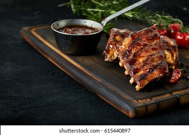 Spicy rack of spare ribs with marinade in a small saucepan and a red hot chili pepper served on an old wood chopping board in a restaurant , close up view with copy space