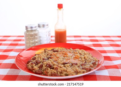 Spicy Red Beans And Rice On Colorful Plate With Louisiana Hot Sauce On Red Plaid Tablecloth And White Background With Copy Space.