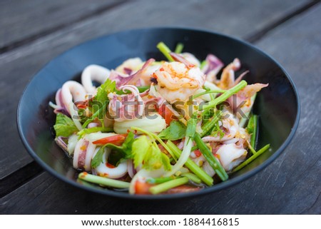Spicy sea food (boiled shrimp and squid) is mixed with fresh vegetable (onion and celery) and spicy sauce as Thai food style.