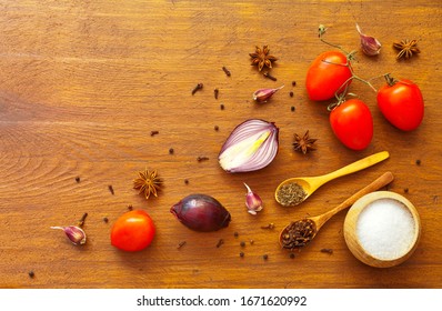 Spicy seasonings for cooking savoury foods useful in viral diseases. Garlic, onion, anise, pepper, cloves, caraway seeds, coarse salt and  tomatoes on wooden background. Flat lay, copy space, close-up - Powered by Shutterstock