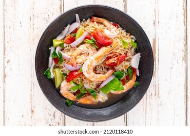 spicy and sour instant noodle salad with shrimp, minced pork, tomato, lime, red onion, shallot and celery in black ceramic plate on white old wood texture background, top view, Thai food, Yum Mama - Shutterstock ID 2120118410