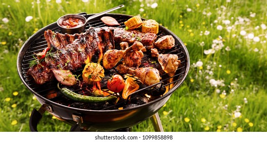 Spicy spare ribs, assorted veggies and chicken drumsticks grilling on a portable barbecue outdoors in a spring meadow with dandelions in a panorama format - Powered by Shutterstock