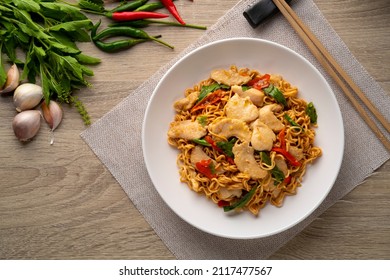 Spicy stir fried instant noodle with sliced chicken breast and thai basil leaves in white plate.top view