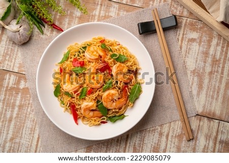 Spicy stir fried instant noodle with shrimps and thai basil leaves in white plate.Top view