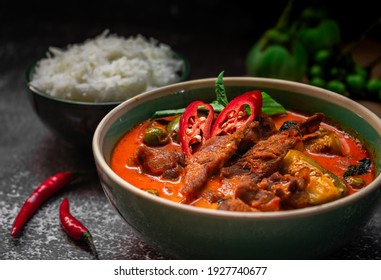 spicy thai curry with pork meat serving with rice and decorating with herbal vegetable ingredients like chili and eggplant on rustic background - Thai food - Shutterstock ID 1927740677