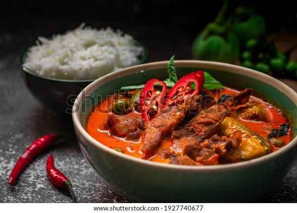 spicy thai curry with pork meat\
serving with rice and decorating with herbal vegetable ingredients\
like chili and eggplant on rustic background - Thai\
food
