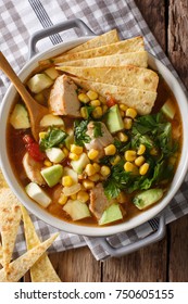 spicy tortilla soup with chicken, cilantro, tomatoes, avocado and corn close-up on the table. Vertical top view from above