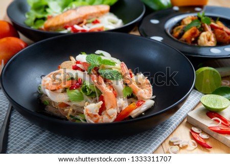 Spicy vermicelli salad with salmon and seafood served on black plate on wooden table, Thai cuisine. - Image