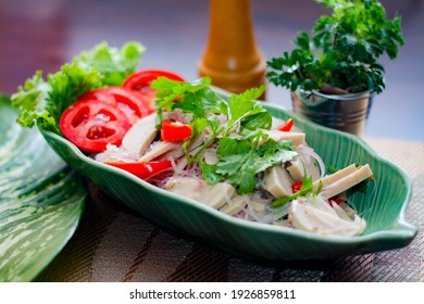 Spicy vietnamese sausages salad placed in a leaf-shaped green plate. With onion, garlic, red pepper on a black wooden table