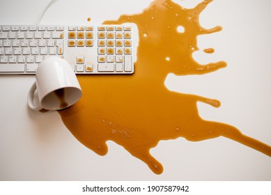 Spilled black coffee on a computer keyboard at a white table