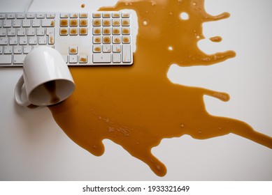Spilled black coffee on a computer keyboard at a white table