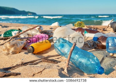 Spilled garbage on beach of big city. Empty used dirty plastic bottles. Dirty sea sandy shore the Black Sea. Environmental pollution. Ecological problem. Bokeh moving waves in the background  