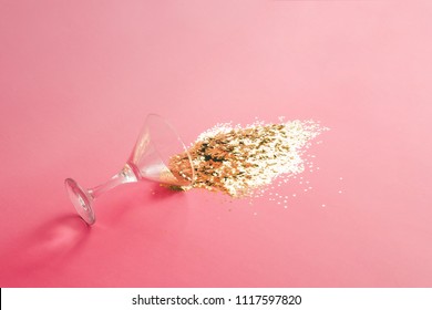 Spilled Martini Glass Full Of Gold Glitter On Pink Background. Creative Minimal Party Concept.