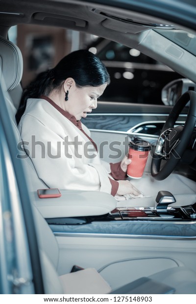 Spilling coffee. Dark-haired\
overloaded businesswoman wearing beige coat spilling her coffee on\
it