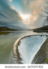 Spillway Waterfall at Sunset with Dramatic Sky - A wide-angle shot of a dam spillway with water cascading into a waterfall under a magnificent, cloudy sky at sunset.